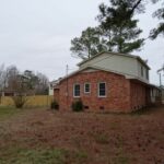 Fenced Brick Home with Plants, Trees, and Empty Land