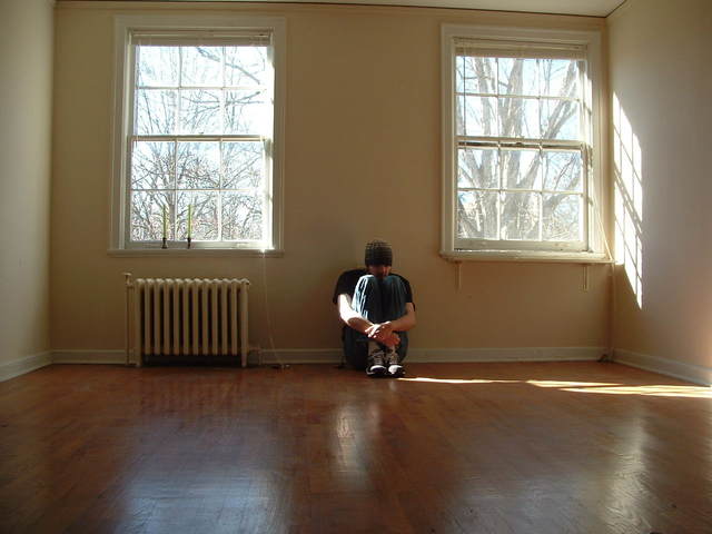 A Man Sitting Alone in the Corner on the Floor and Wall with Two Windows