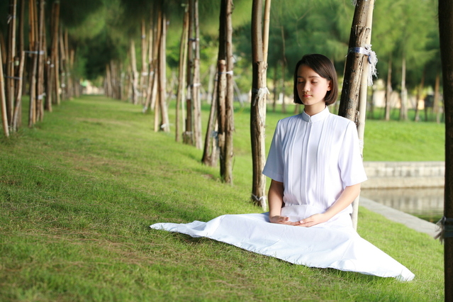 A Young Woman in White Dress Meditating in a Park