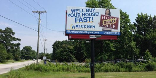 Advertisement of Blue Hen Homebuyers with a Billboard on a Pole